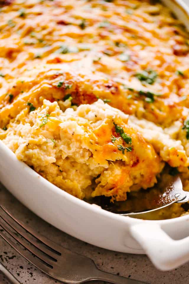 Close-up image of a cheesy Chicken and Cauliflower Rice Casserole with a spoon scooping out a serving of the casserole.