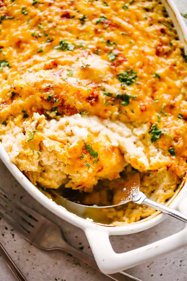 A serving spoon scooping out cauliflower rice casserole from a baking dish.