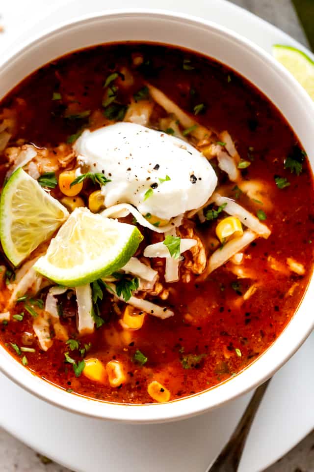 Soup served in a bowl and garnished with lime slices, a dollop of sour cream, and shredded cheese.