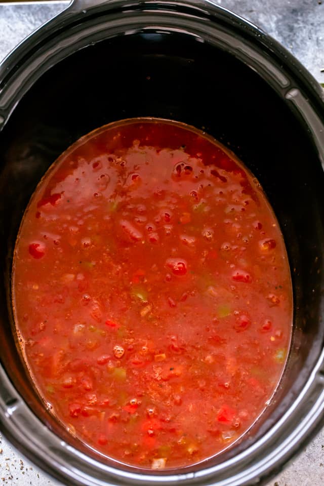 This slow cooker chicken enchilada soup is filled with classic enchilada flavors, with shredded chicken, corn, beans, and red enchilada sauce. The broth ingredients for chicken enchilada soup combined in a slow cooker.