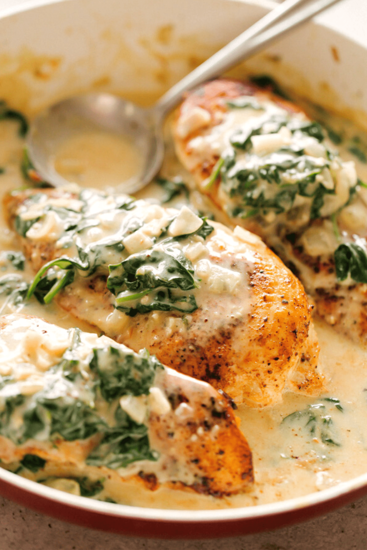 side shot of three chicken breasts in a skillet, topped with creamed spinach.