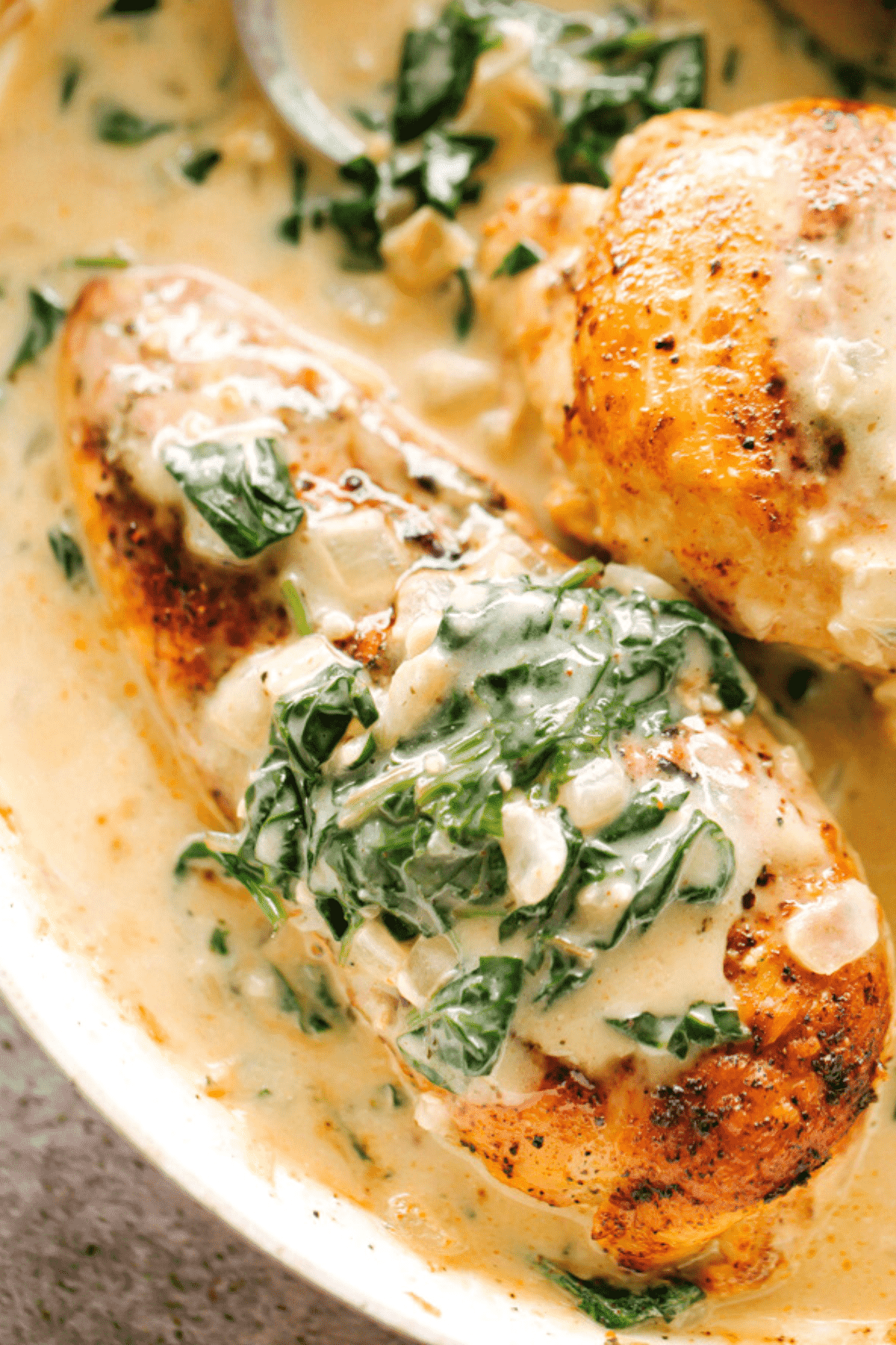 close up shot of chicken breasts in a skillet, topped with creamed spinach.
