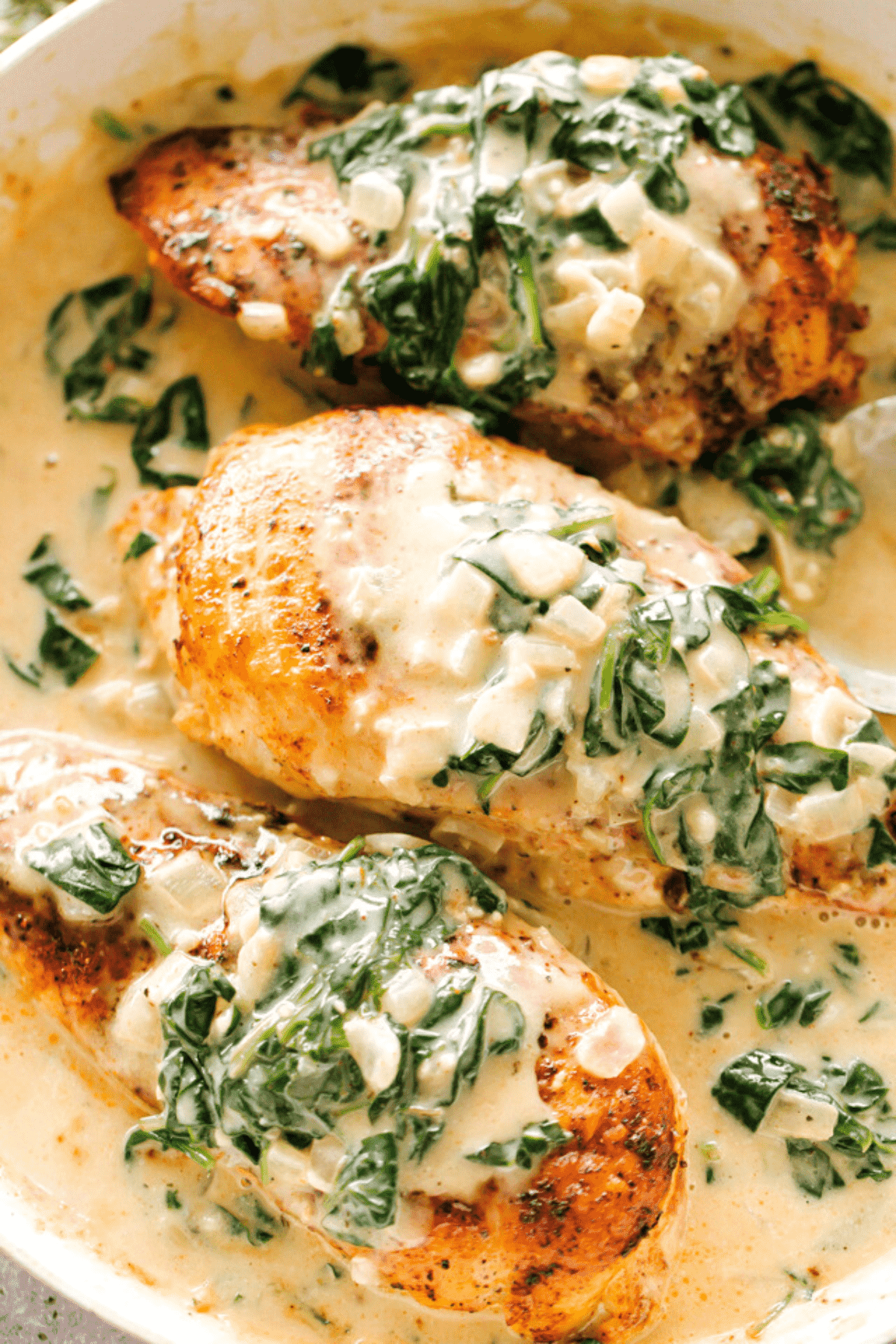 Overhead view of three chicken breasts in a skillet, topped with creamed spinach.