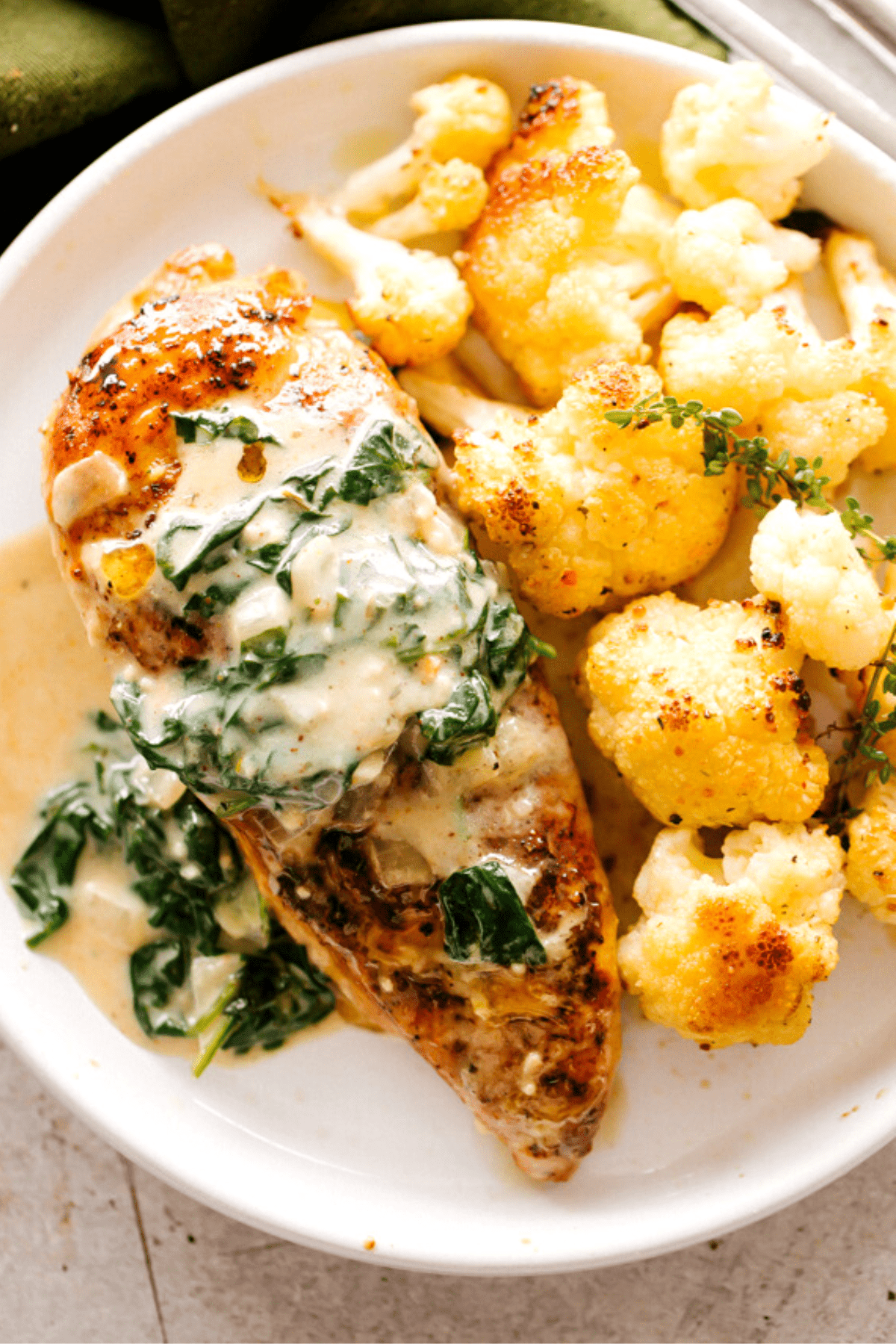overhead shot of creamed spinach topped chicken breasts served on a dinner plate with cauliflower on the side.