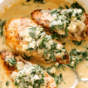 overhead shot of three chicken breasts in a skillet, topped with creamed spinach.