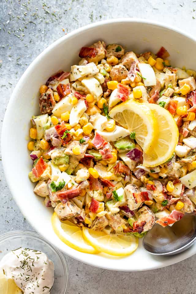 A large salad bowl filled with a mixture of avocados, diced chicken, eggs, bacon, and corn.