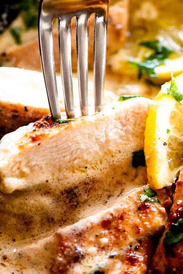 Close up of a fork picking up a slice of chicken breast covered with lemon parmesan sauce.