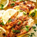 Lemon parmesan chicken in a skillet with creamy sauce, topped with lemon slices and fresh herbs.