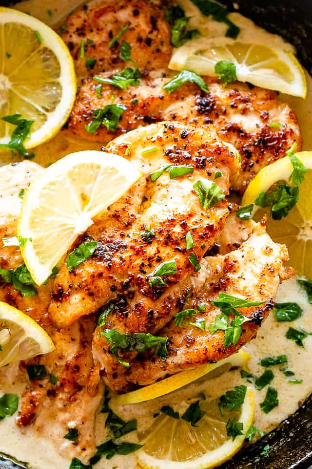 chicken breasts in creamy sauce, topped with lemon slices and fresh herbs.