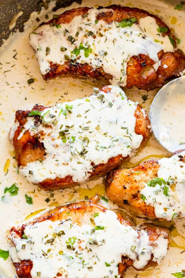 Overhead view of four pork chops smothered in cream sauce, in a pot with more sauce. 