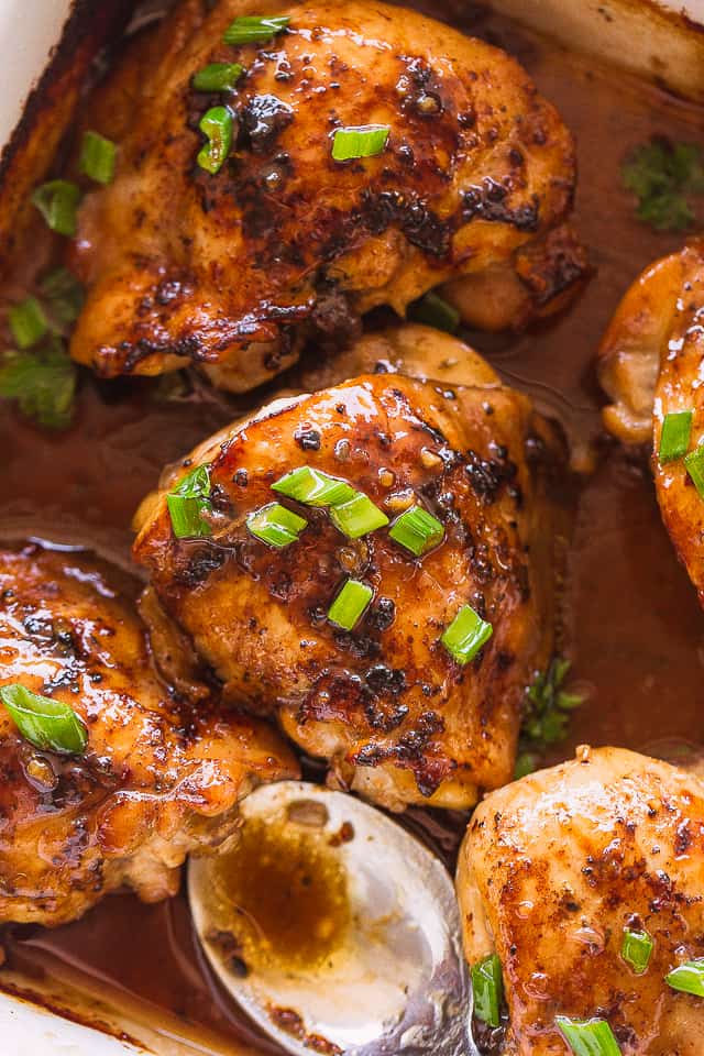 Close-up photo of Oven Baked Chicken Thighs topped with a juicy marinade and sliced green onions.