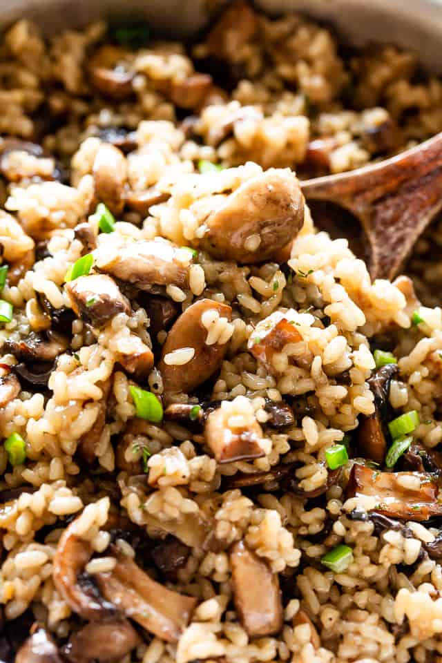 Close up of a wooden spoon in a serving of mushroom rice with green onions. 