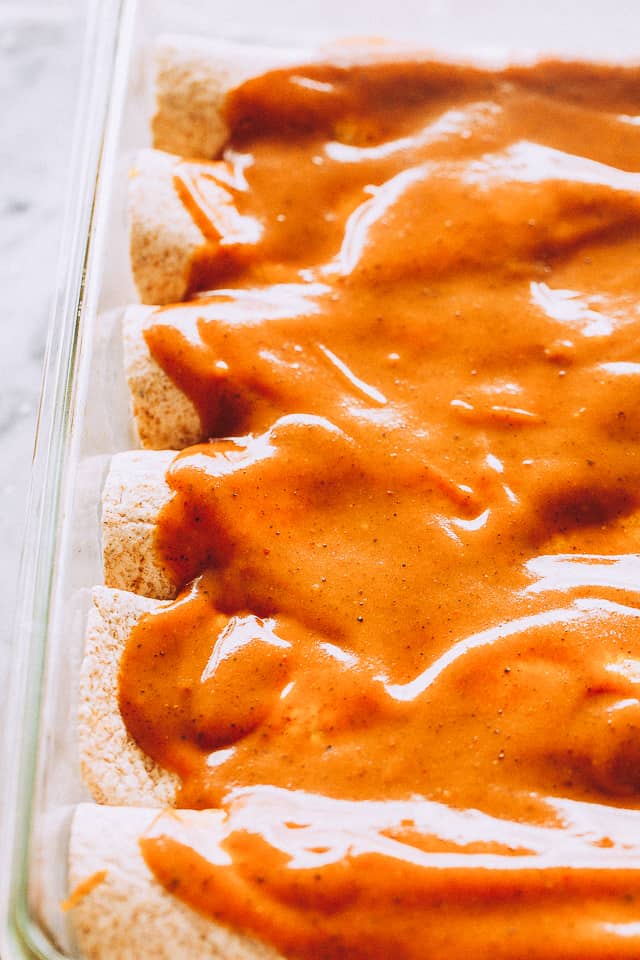 Enchiladas covered with enchilada sauce in a baking dish.