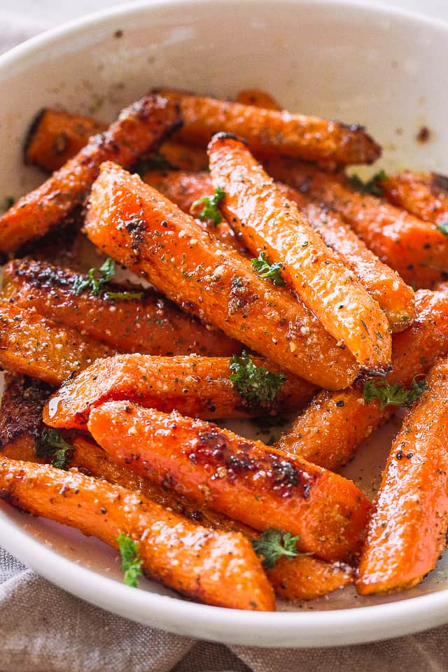 Roasted Carrots tossed with butter, garlic, and parmesan cheese and served in a big white bowl.