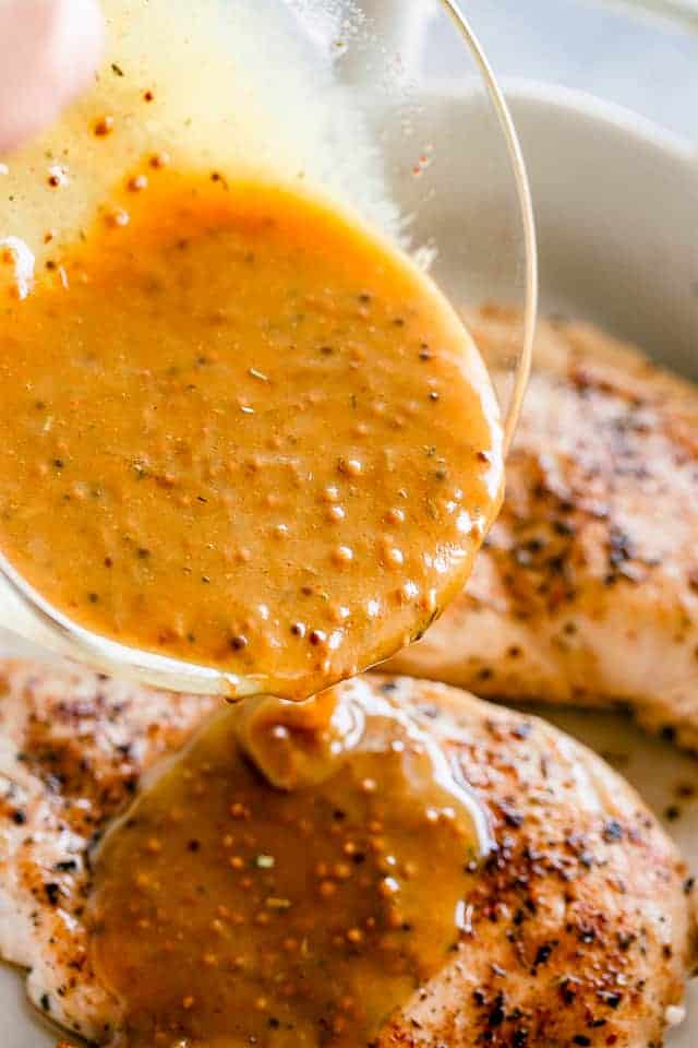 Pouring Honey Mustard Sauce over browned chicken breasts.