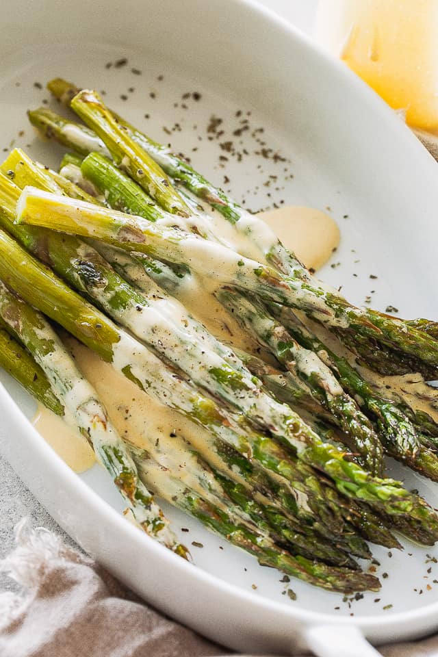 Roasted asparagus in a white dish covered with sauce