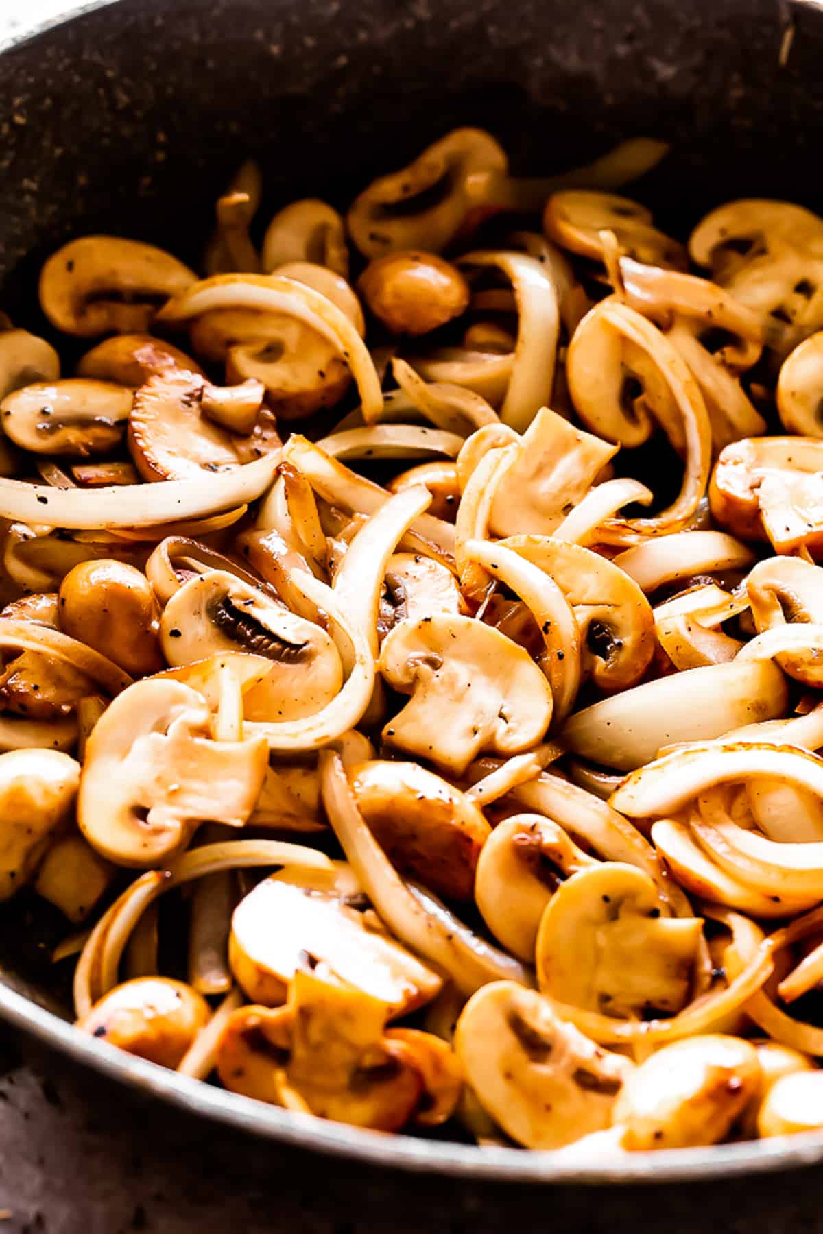 cooking sliced onions and sliced mushrooms in a dark skillet.