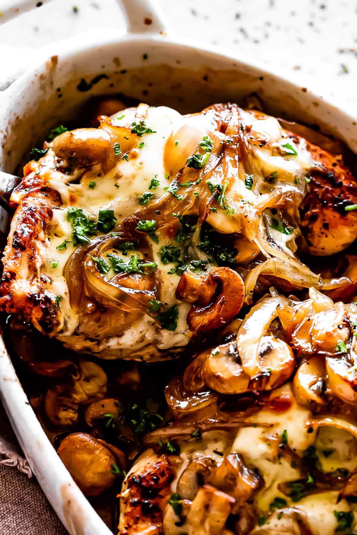 close up shot of chicken breasts in an oval baking dish topped with mushrooms, onions, and melted cheese.