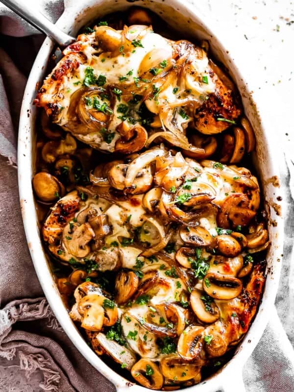 overhead shot of three chicken breasts in an oval baking dish topped with mushrooms, onions, and melted cheese.