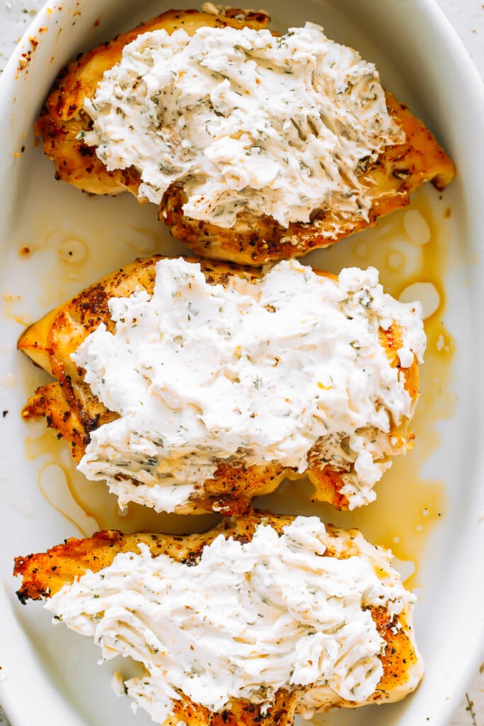 three chicken breasts in a baking dish, topped with ranch and cream cheese.