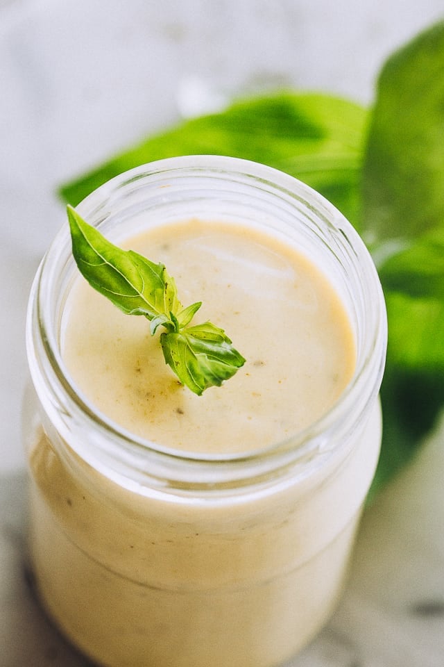 A jar of creamy sauce, garnished with a sprig of fresh basil leaves.