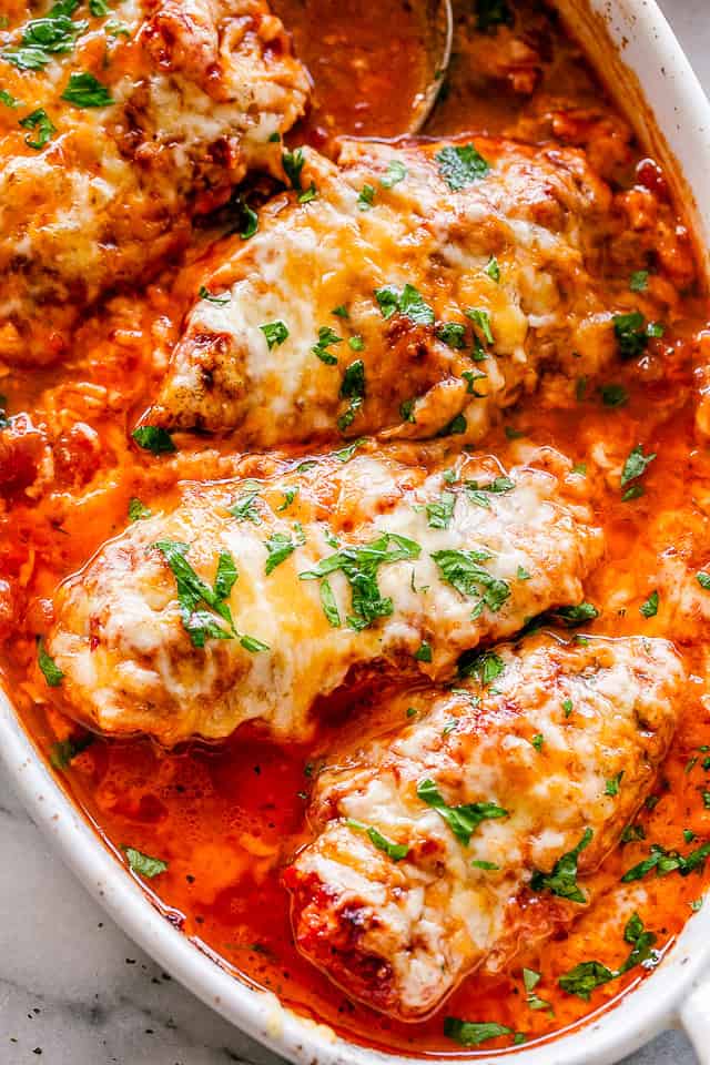 Overhead close-up of four baked chicken breasts arranged in a baking dish with tomato salsa.