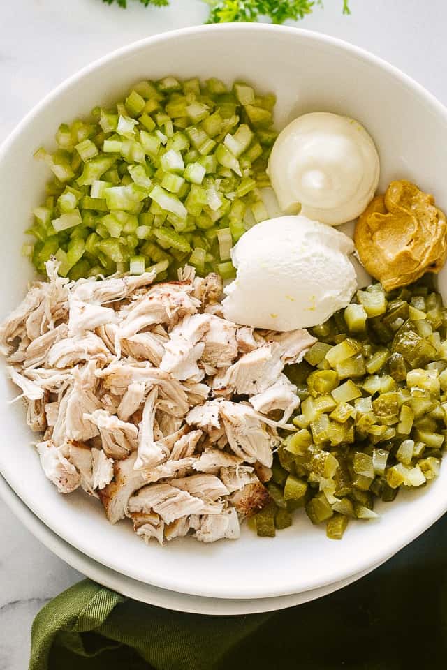 Dill pickles, shredded chicken, celery, and mayo dressing inside a salad bowl.