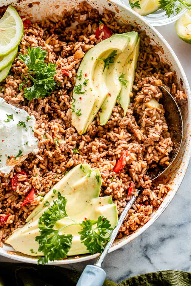 Cooked beef and rice in a skillet, topped with avocados.