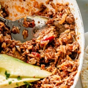 Scooping out ground beef and rice from a skillet.