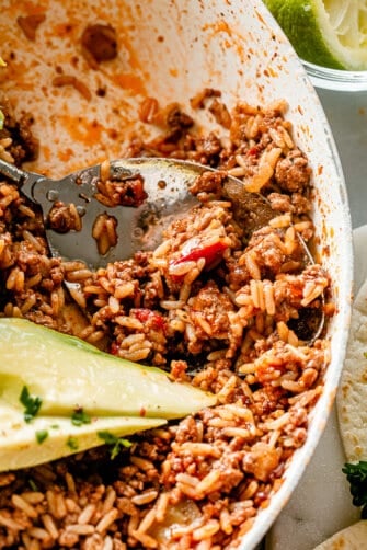 Scooping out ground beef and rice from a skillet.