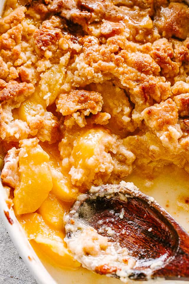 Peach Cobbler in a baking dish with a wooden spoon.