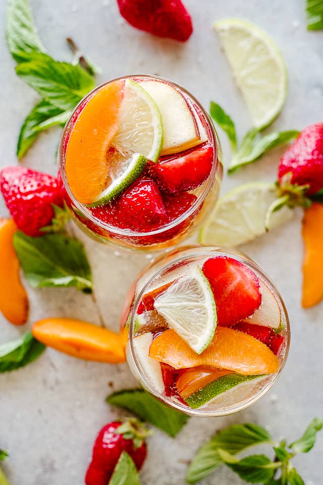 Two drinking glasses filled with white wine and fruits.