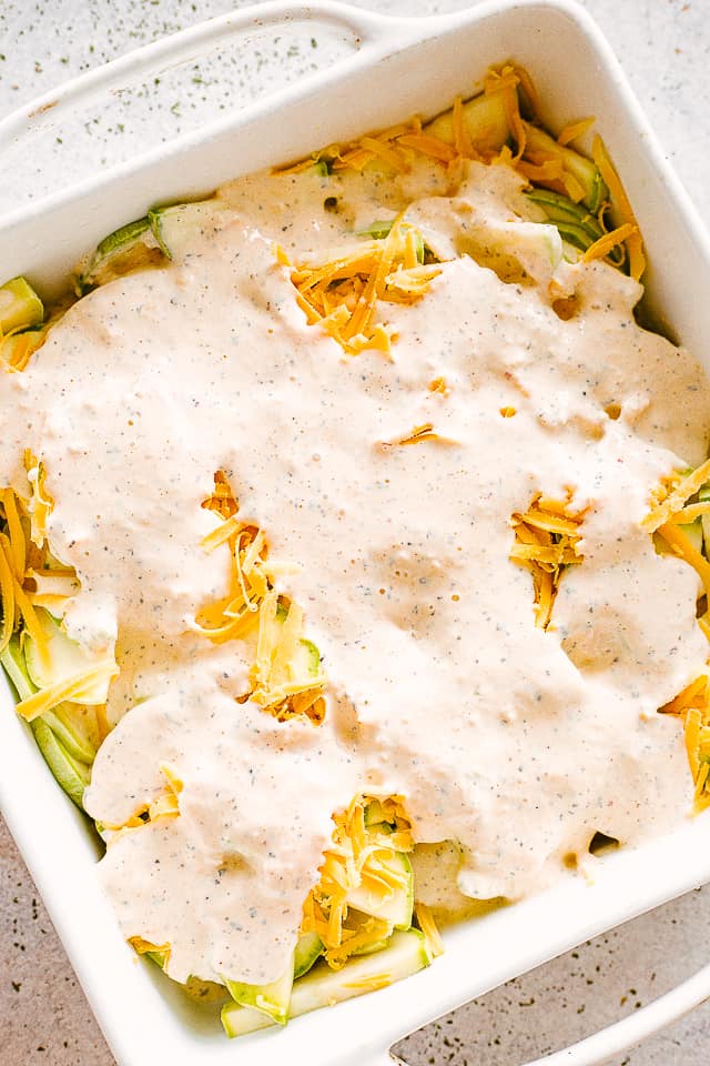 Layers of fresh zucchini slices, cheese, and cream in a baking dish.