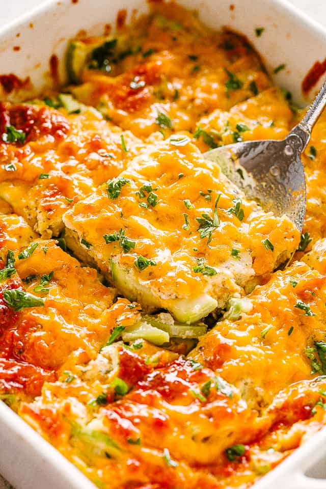 Lifting up a slice of zucchini casserole from a baking dish.