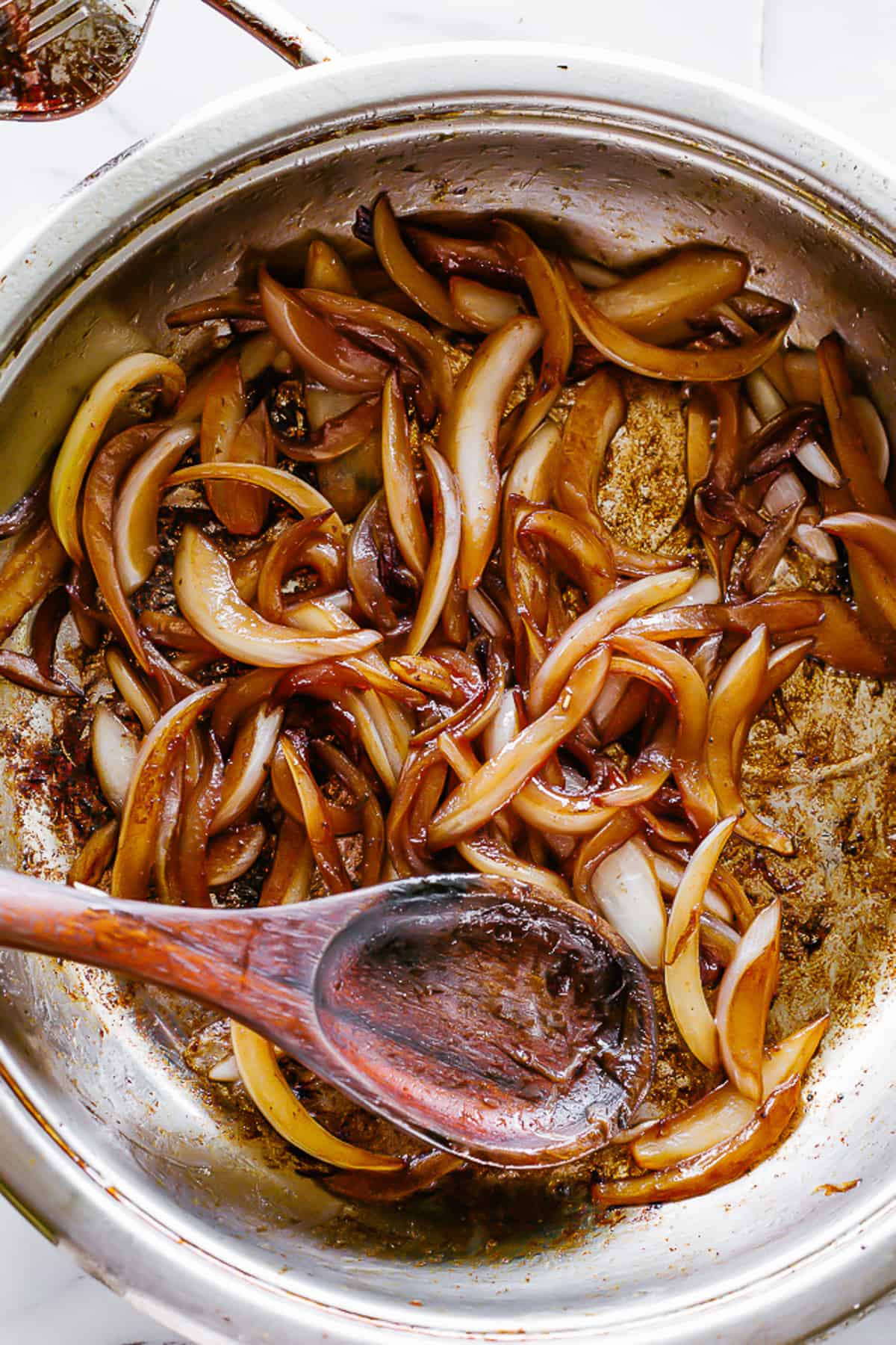 Onions caramelizing in a stainless steel skillet.