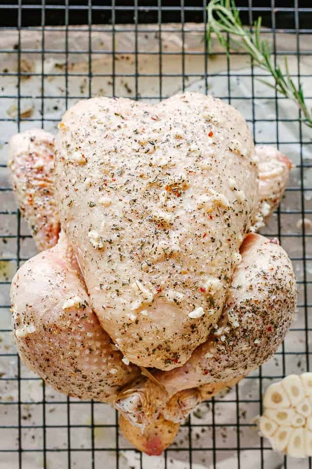 Uncooked whole chicken rubbed with butter, garlic, and seasonings on a rack.