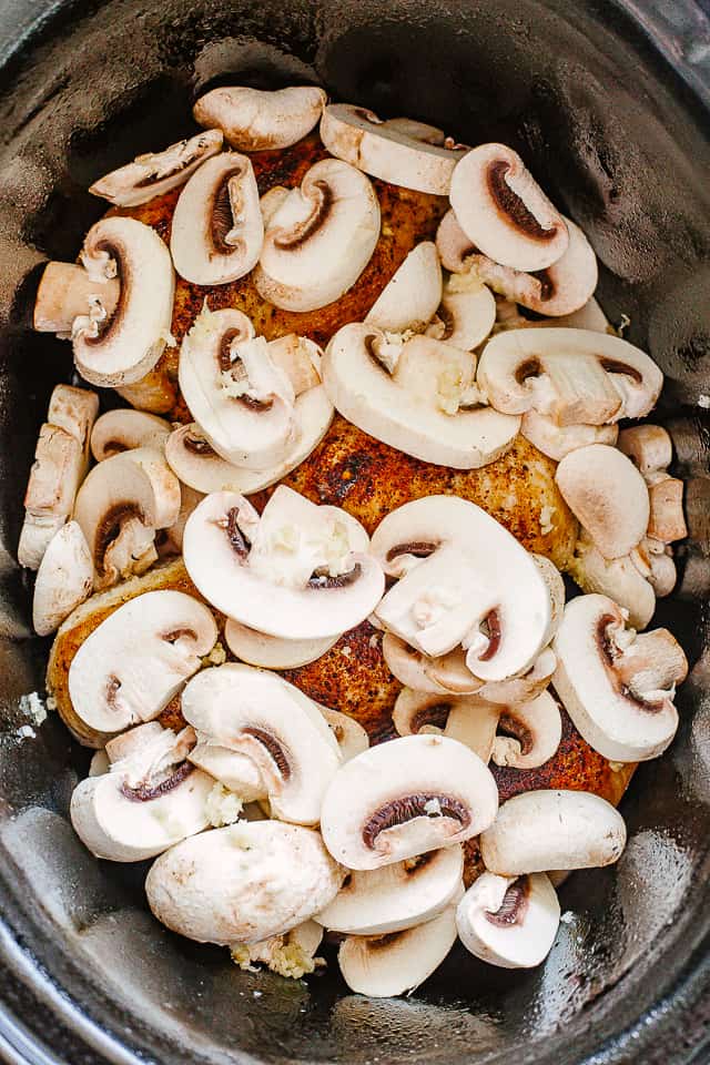 Sliced mushrooms arranged over chicken breasts in a slow cooker.