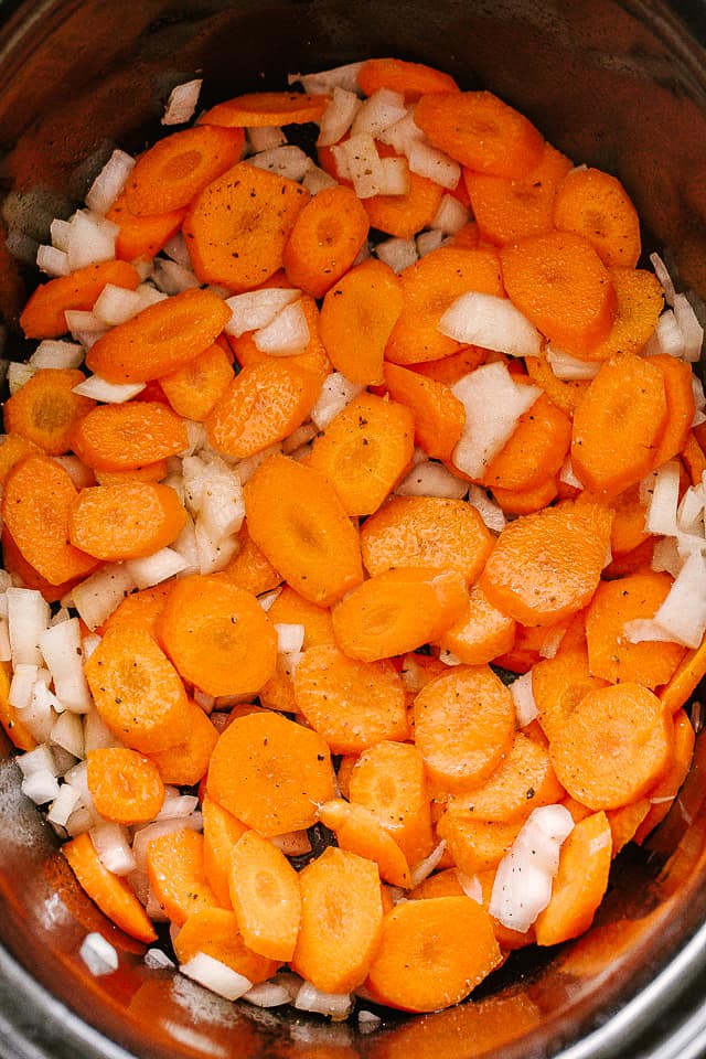 Sliced carrots and onions inside a slow cooker.