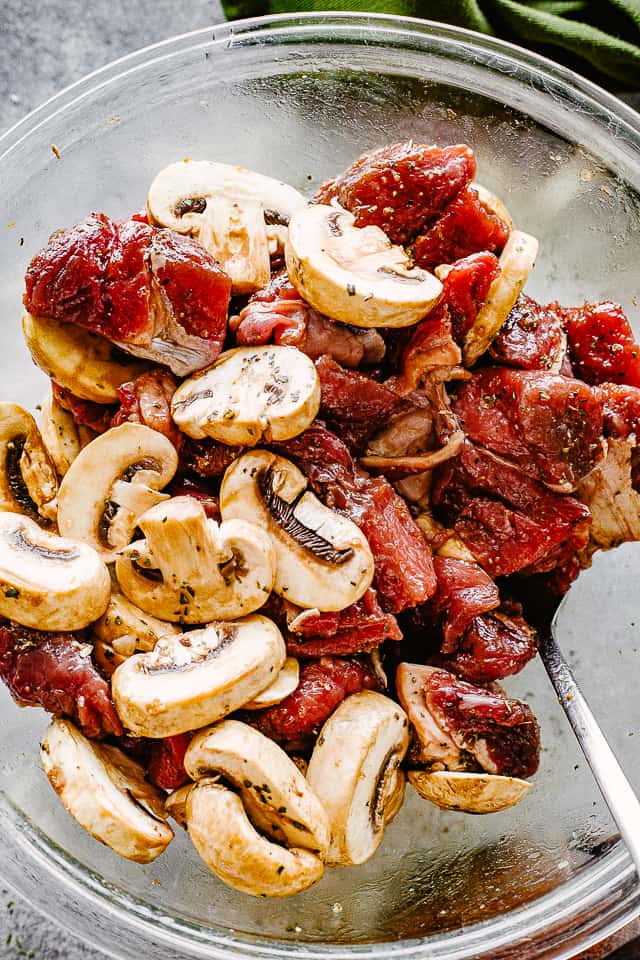 Raw steak bites and mushrooms in a bowl.