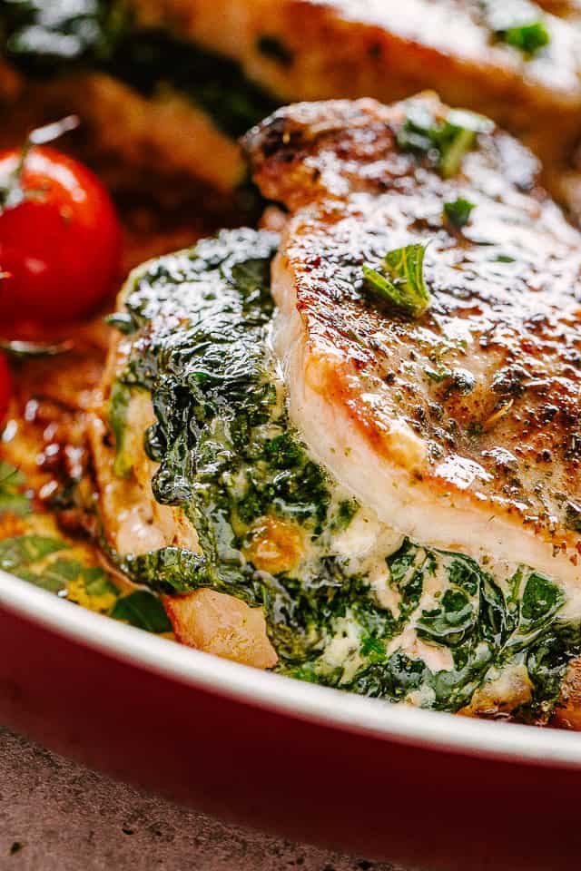 Spinach stuffed pork chops next to cherry tomatoes on a white plate with a fork.