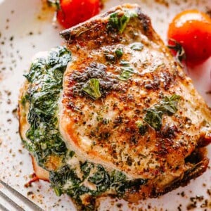 Spinach stuffed pork chops on a white plate with a fork.