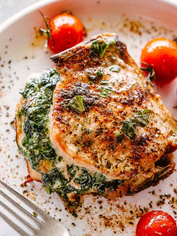 Spinach stuffed pork chops on a white plate with a fork.