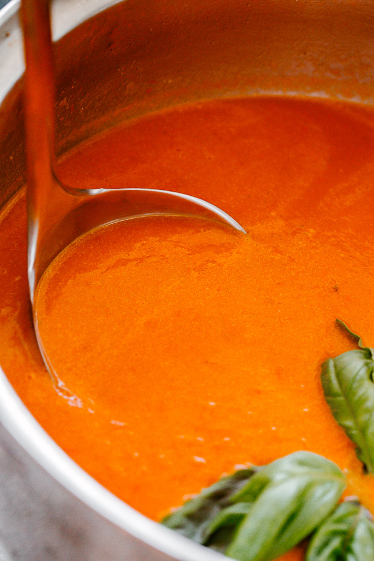 A ladle inside a pot with tomato soup.