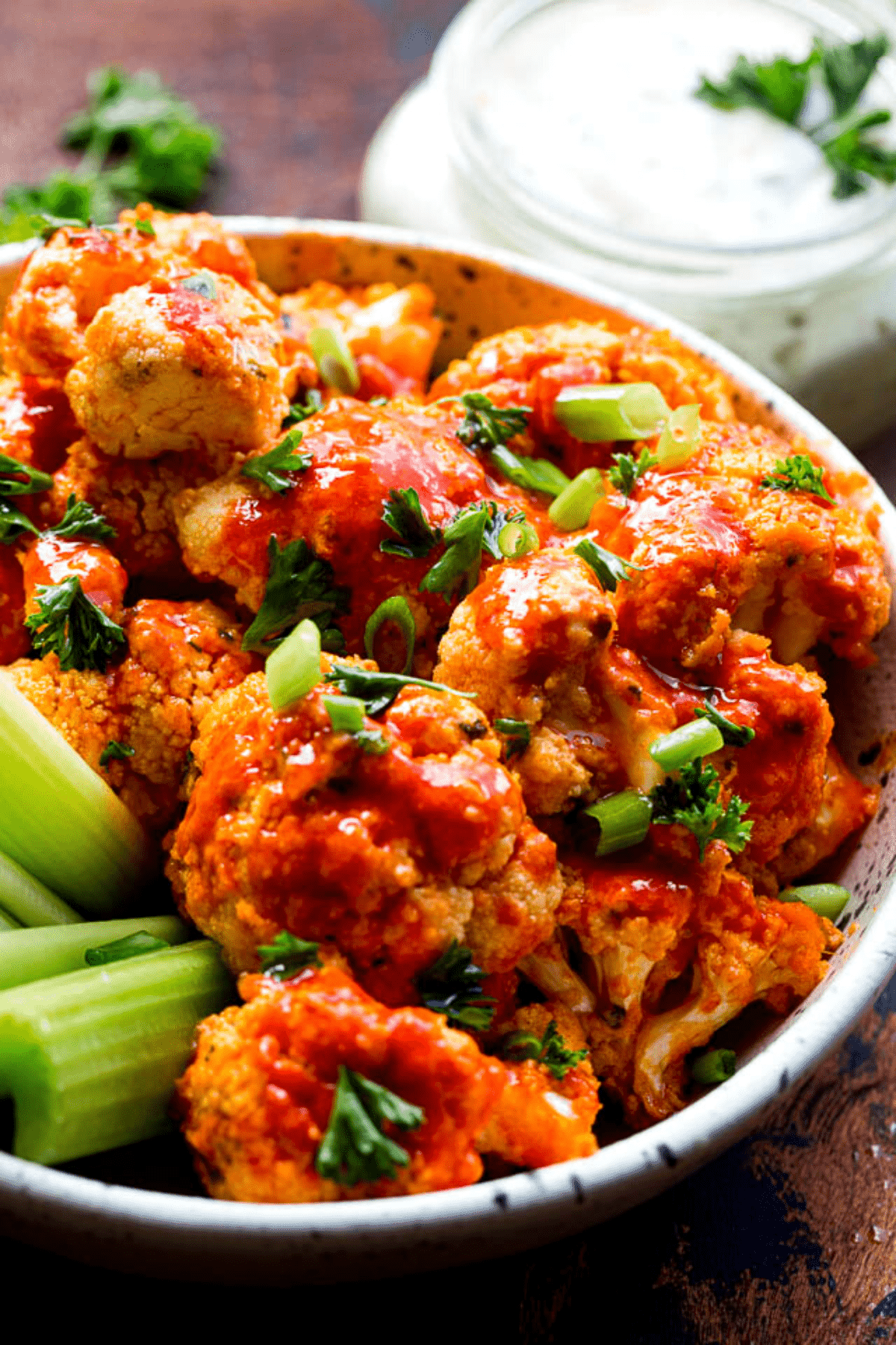 Cauliflower florets topped with hot sauce and served in a bowl with celery sticks.