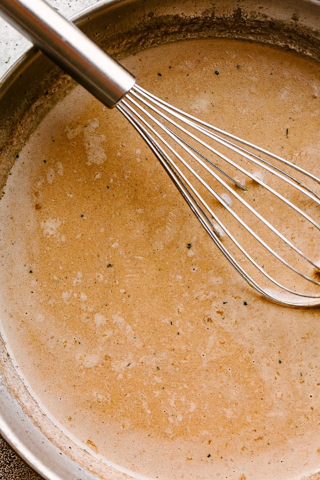 Chicken Lazone cream sauce in a skillet with a whisk.