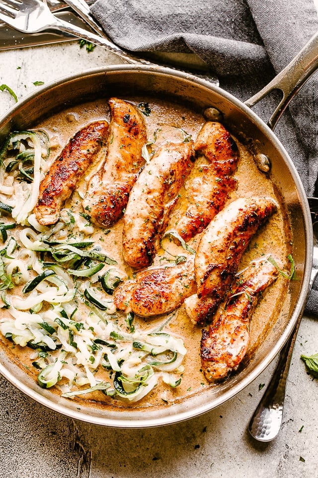 A skillet with chicken tenders in a cream sauce with zucchini noodles.
