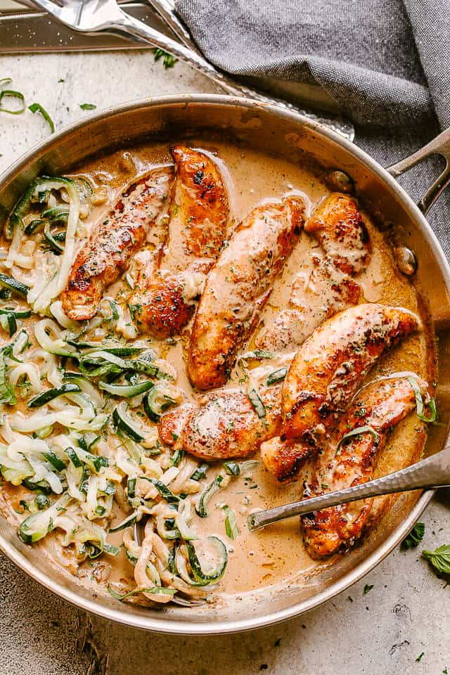 Chicken tenders cooked in a skillet with cream sauce and zoodles.