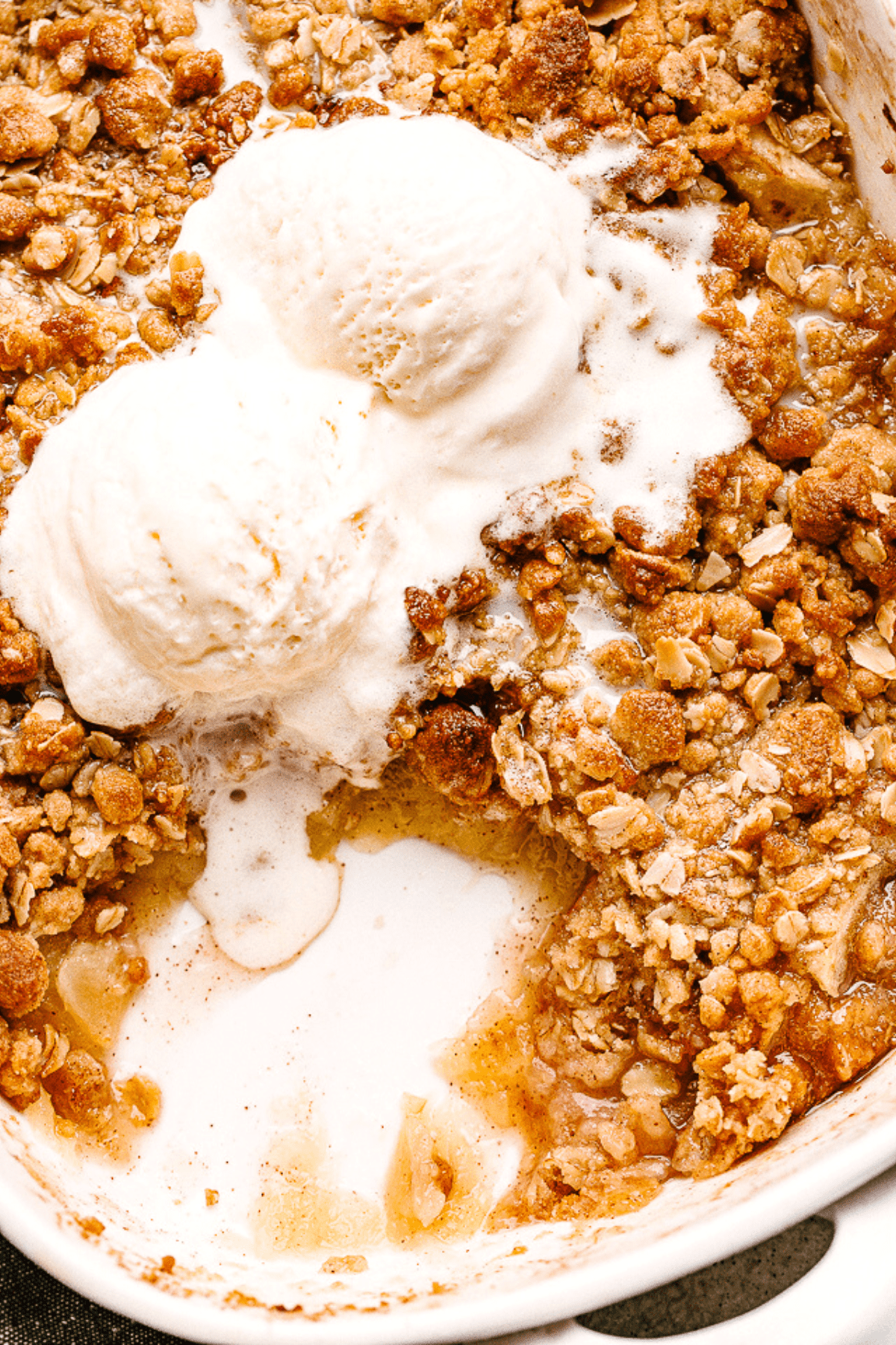 Apple Crumble is the best dessert for apple season! It’s a favorite among everyone with its sweet, caramelized apple filling and perfectly crumbly topping. Baked Apple Crumble in a white baking dish, topped with two scoops vanilla ice cream.