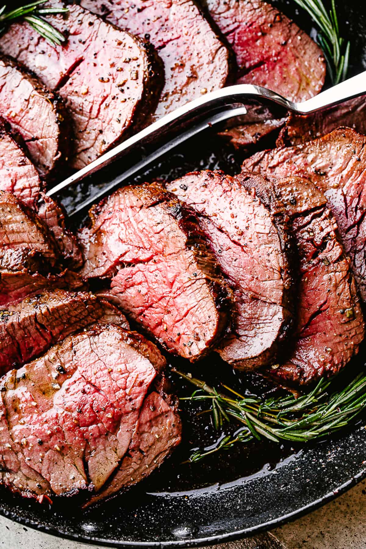 Sliced beef tenderloin with a serving fork placed on top.