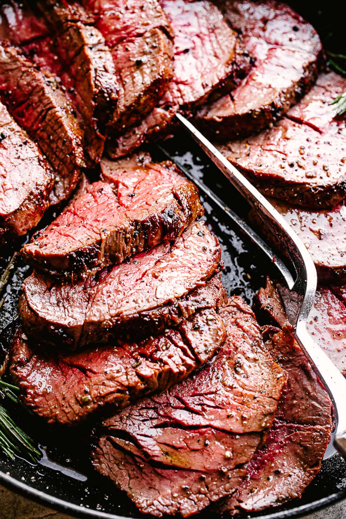 Make the best roasted beef tenderloin with a simple garlic and herb crust! This beef tenderloin roast turns out perfectly juicy and tender every time! Sliced beef tenderloin with serving fork.